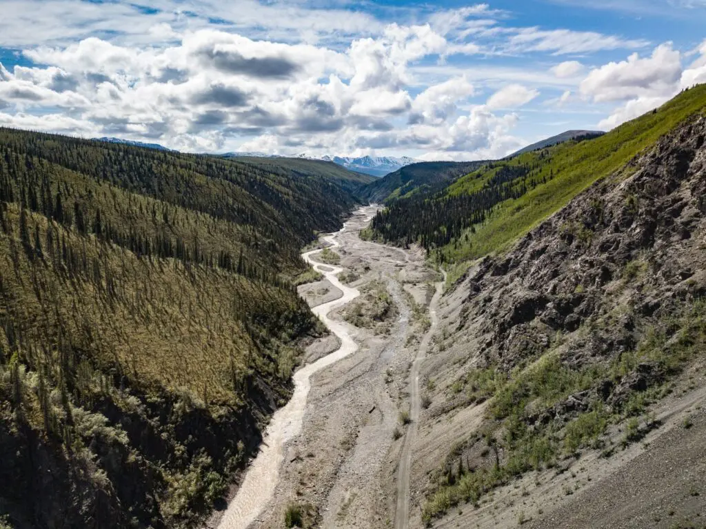 Breathtaking aerial shot of a winding river through a lush mountain valley under a blue sky.