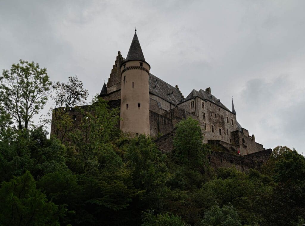 A striking view of Vianden Castle in Luxembourg, nestled among lush greenery under a cloudy sky.