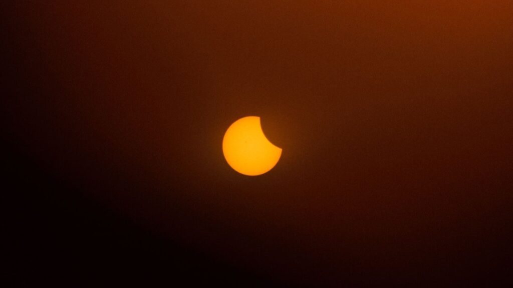 A captivating partial solar eclipse with an orange background in the twilight sky.