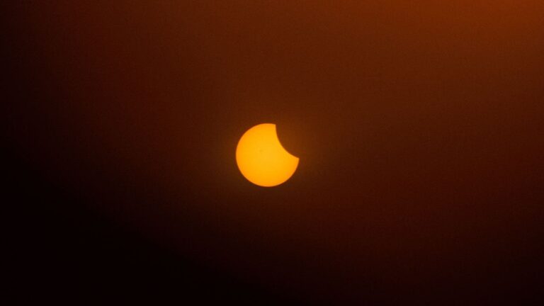 A captivating partial solar eclipse with an orange background in the twilight sky.