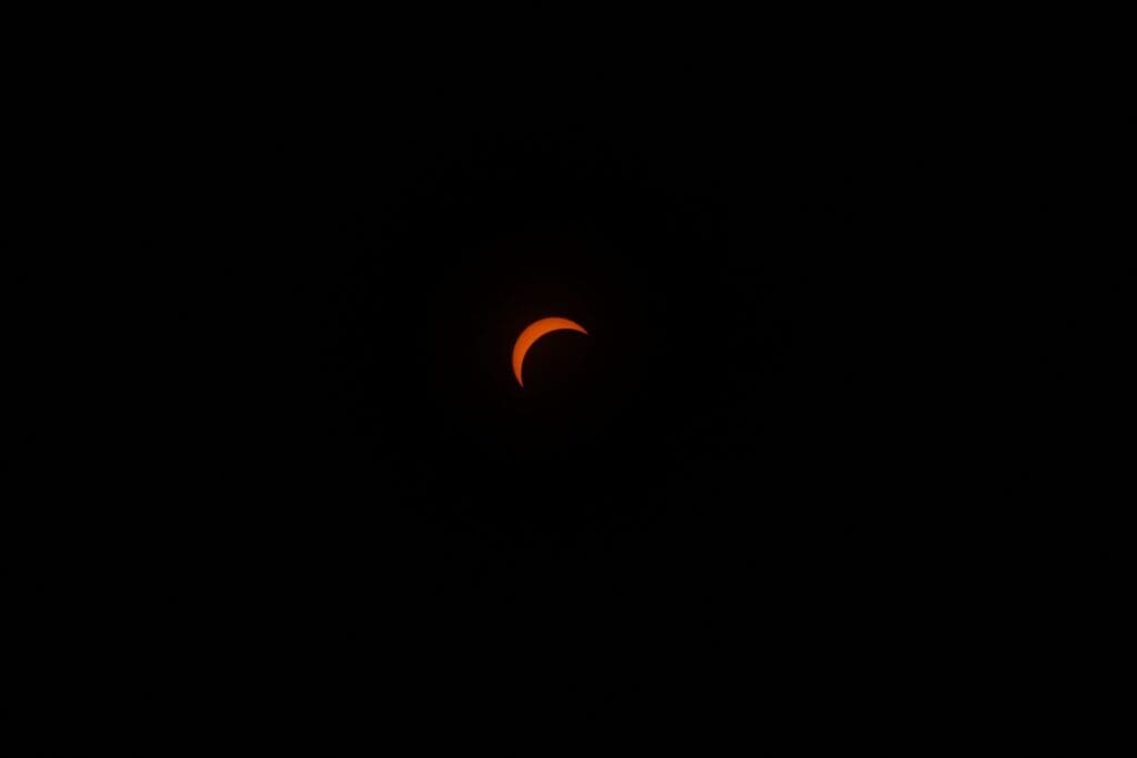 A dramatic view of a solar eclipse, showcasing an orange crescent against a dark sky.