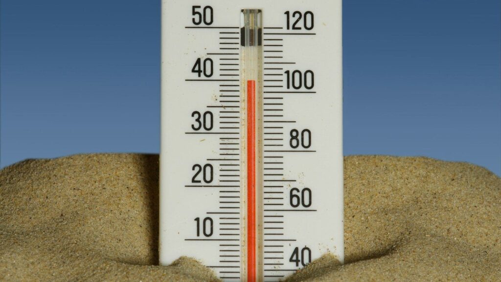 A thermometer in the sand with a blue sky in the background